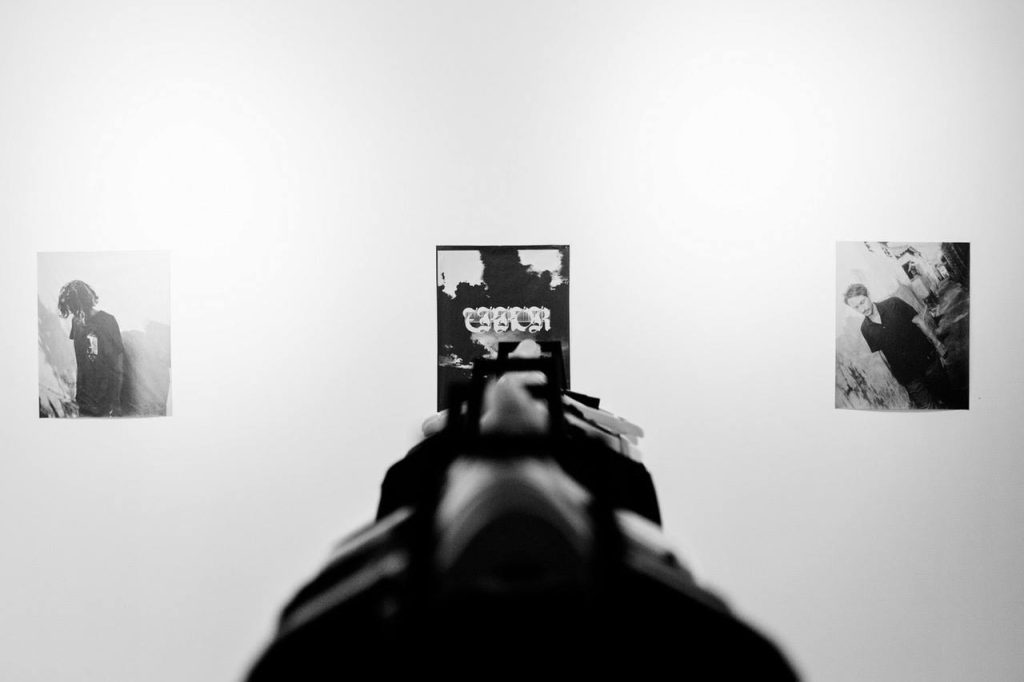View along a gun barrel toward black-and-white photographs at the Former 'Generics' launch at The Slow
