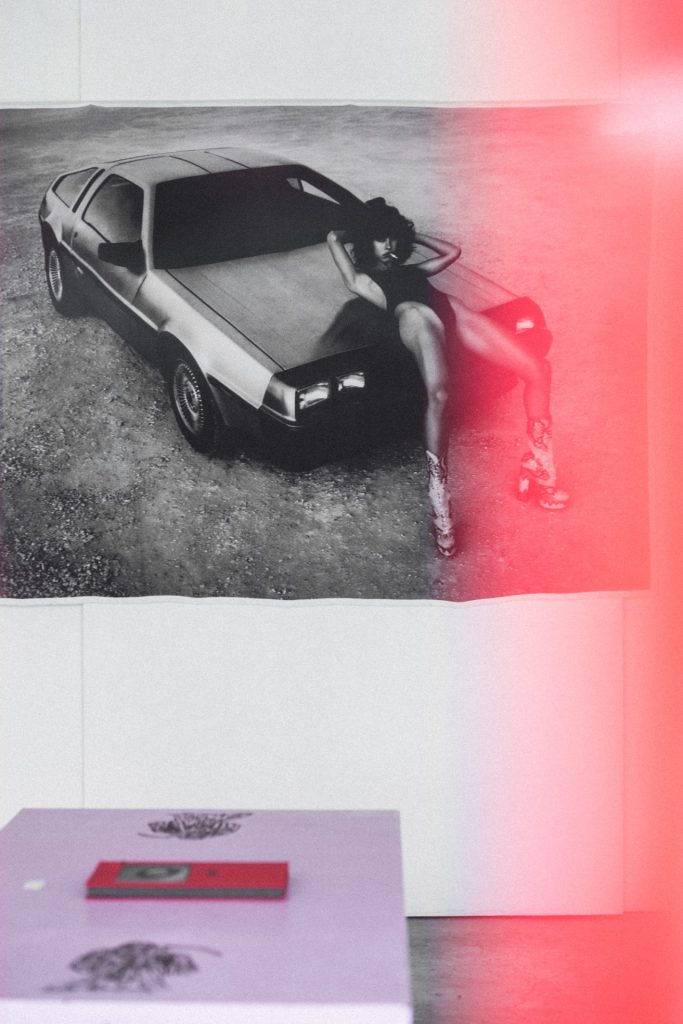 Black-and-white Kate Bellm print of a woman on a DeLorean at the 'Amor' exhibition, The Slow